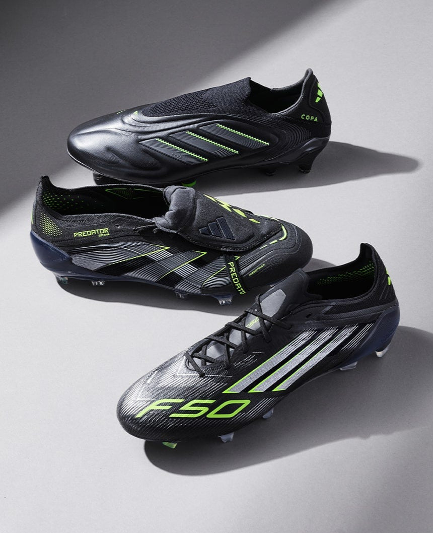Three black soccer cleats with green accents on a gray background